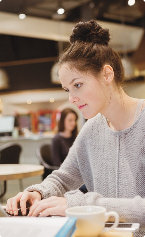 Frau arbeitet konzentriert am Laptop in einem modernen Café mit Tasse Kaffee im Vordergrund
