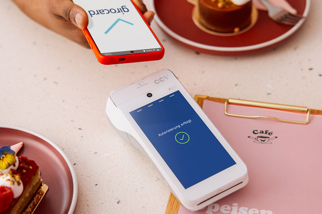 Kontaktlose Bezahlung mit Smartphone an Kartenlesegerät auf Verkaufstresen im Laden