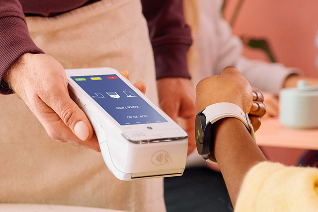Kunde bezahlt kontaktlos mit Smartwatch an mobilem Kartenterminal im Geschäft